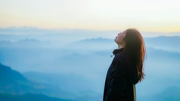 Woman taking a slow deep breath of fresh air above misty blue mountains