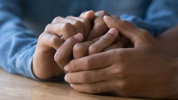 One person's hands gently clasped over another's on a table in support