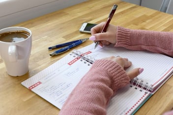Person writing goals in a planner at a sunny desk with a cup of coffee