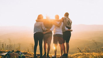 Four friends standing arm in arm together watching the sunset