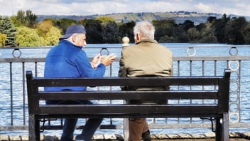 Two men having a supportive conversation on a lakeside bench