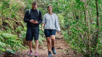 Two friends walking and talking together on a green forest trail