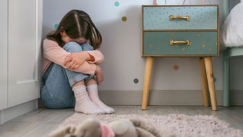 Young girl sitting on her bedroom floor with her head resting on her knees