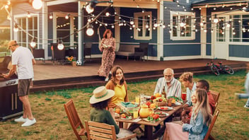 Multigenerational family sharing a backyard dinner together under string lights while one man grills