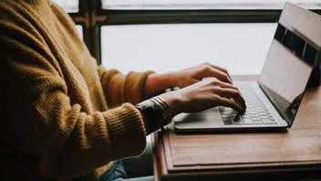Person typing on a laptop at a desk by a bright window, getting started on a task