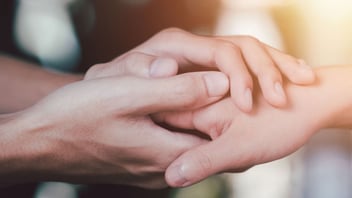 Close up of one person's hands gently holding another person's hand in support
