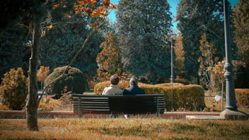 Two people sitting close together on a park bench among autumn trees