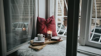 Cozy window seat with a lit candle, warm drink, and book on a winter day