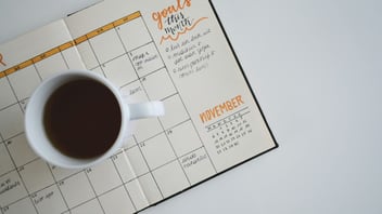 Cup of coffee resting on an open monthly planner with handwritten goals