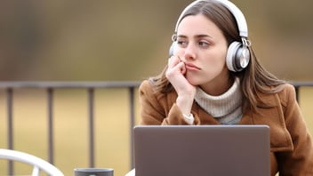 Young woman wearing headphones gazing away from her laptop, lost in thought
