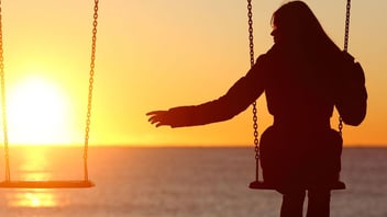 Silhouette of a woman on a swing at sunset beside an empty swing, reaching toward it