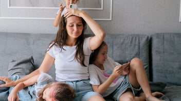 Tired mother sitting on a couch with her two children leaning on her