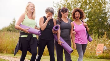 Group of women carrying yoga mats, laughing together on a walk outdoors