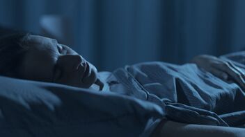 A person lying awake in bed at night in dim blue light