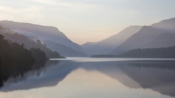 Misty mountain lake at dawn, calm and reflective
