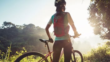Cyclist pausing with a mountain bike on a sunlit trail at sunrise