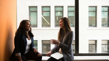 Two women laughing together by a window