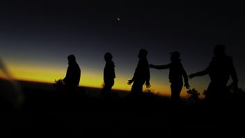 a group of friends walking across a field at sunset