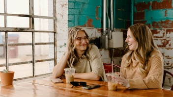 Two adult friends laughing together over coffee at a cafe table