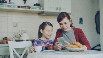 Mother and daughter smiling at a phone together at the breakfast table