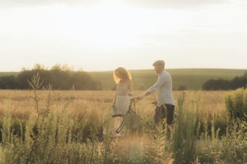 A couple walk a bicycle together through a sunlit golden field