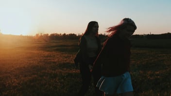 two women walking together on a grass field, supportive companionship