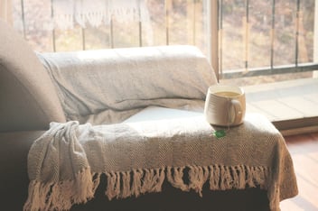 Sunlit couch with a soft blanket and a warm mug of tea by a bright window