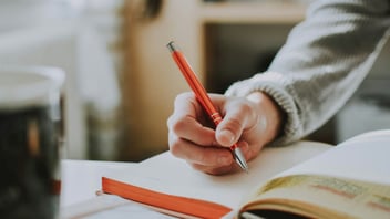 Close up of a hand writing in a journal with an orange pen