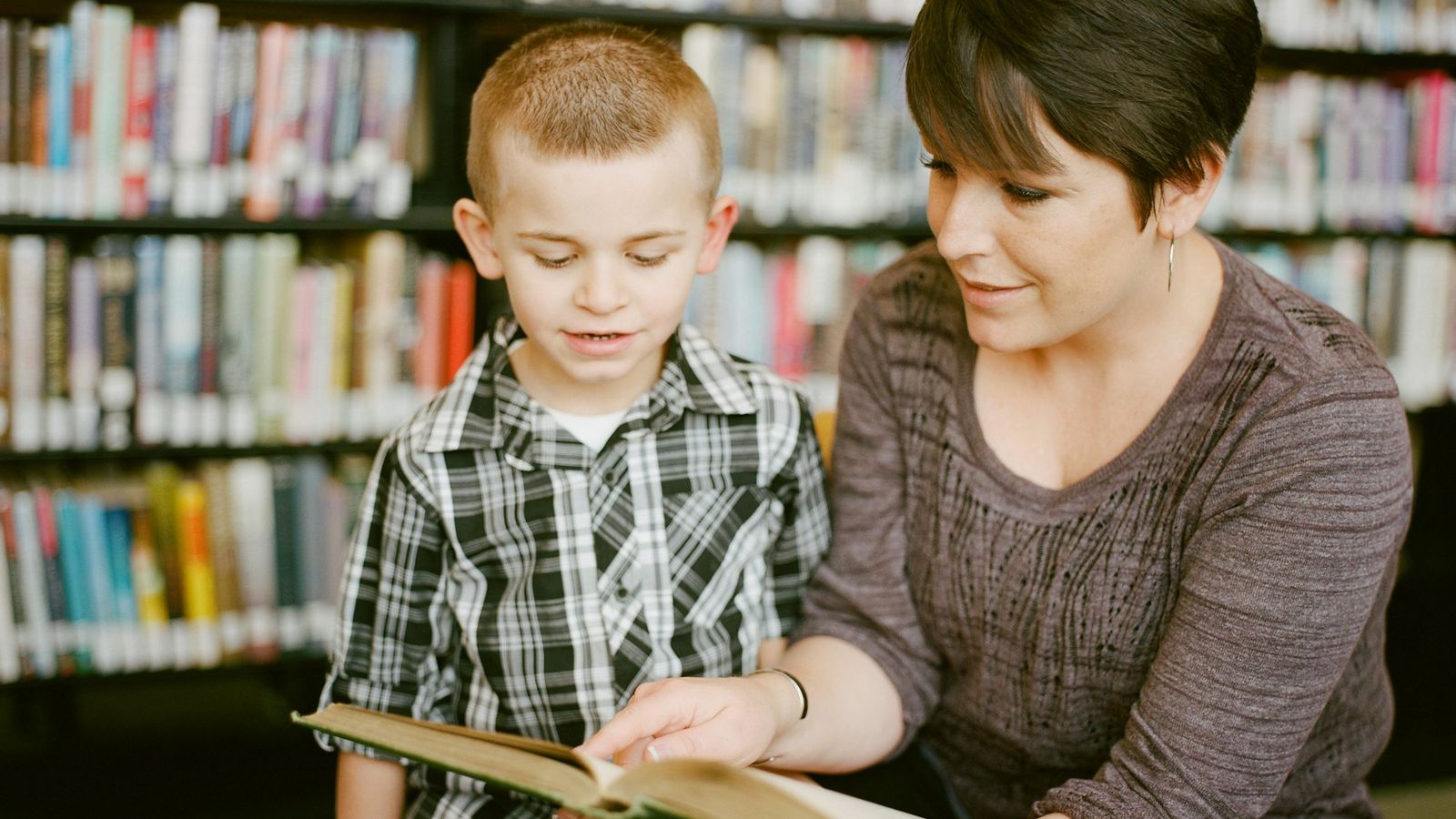 A mother and her young son reading a picture book together in a library