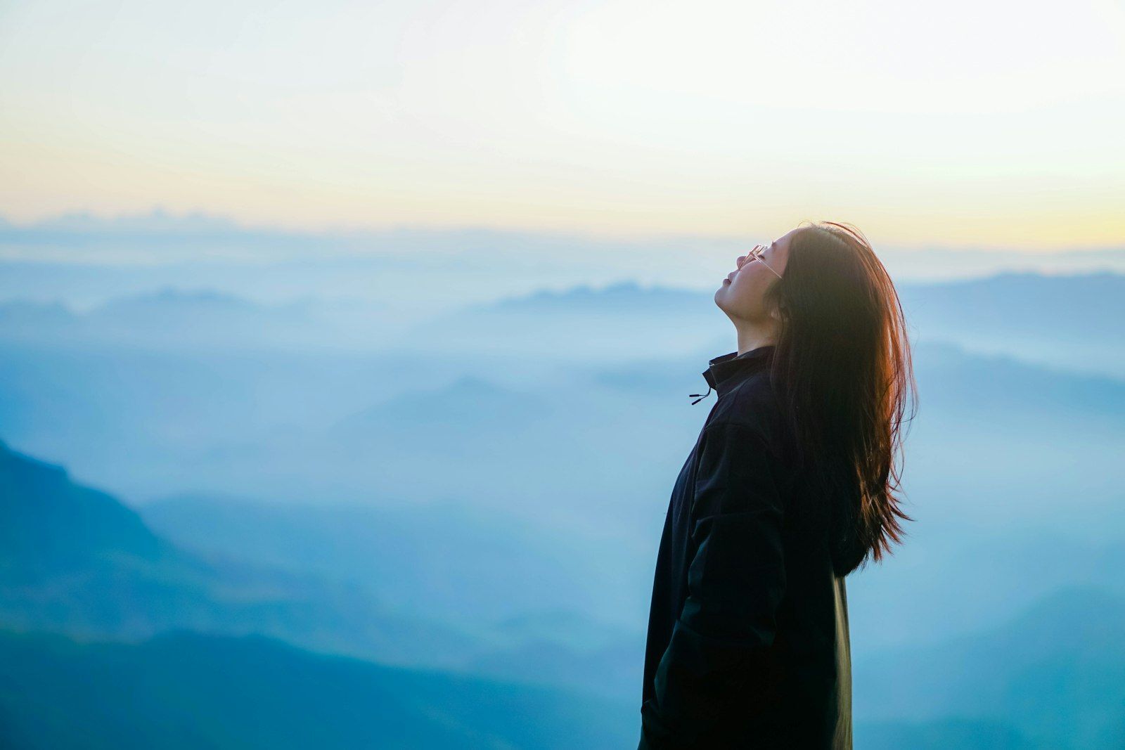Woman taking a slow deep breath of fresh air above misty blue mountains