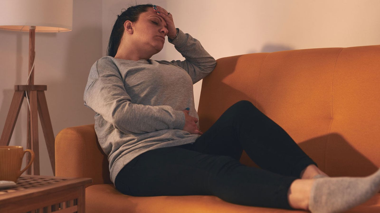 Woman resting on a couch holding her forehead and stomach in discomfort