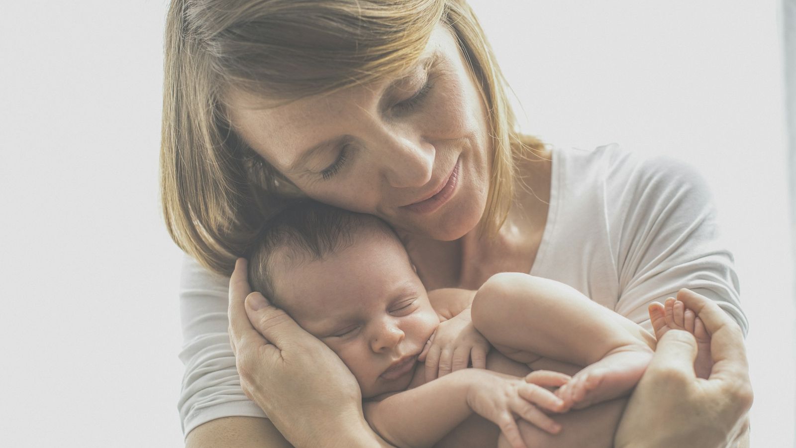 a mother in a white shirt gently carrying her baby