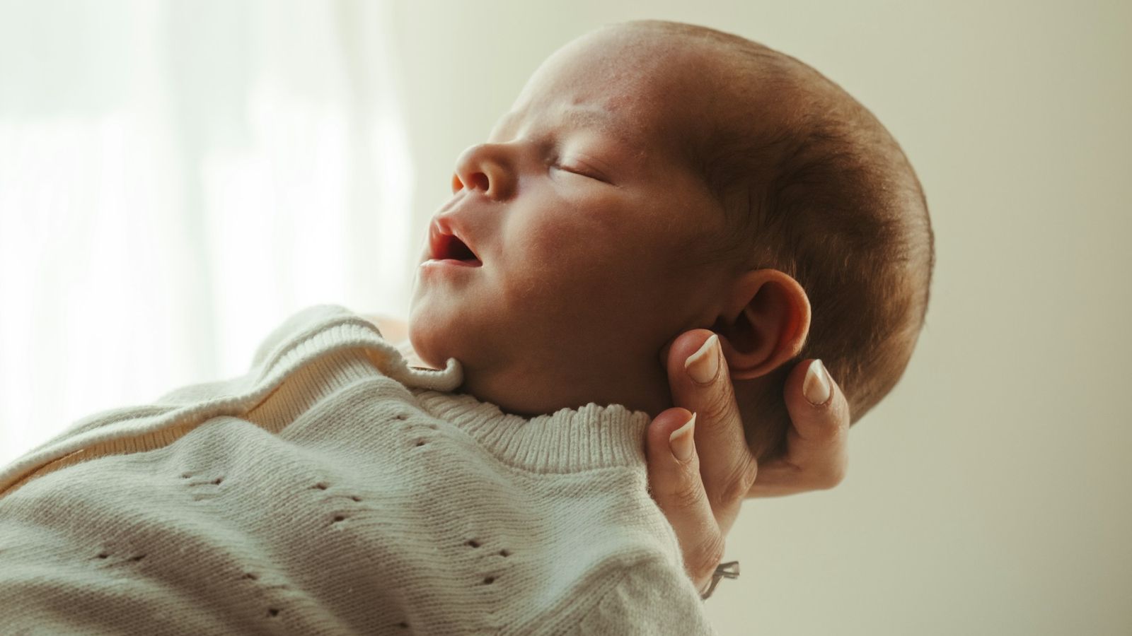 Newborn baby sleeping peacefully in a parents hands in soft window light