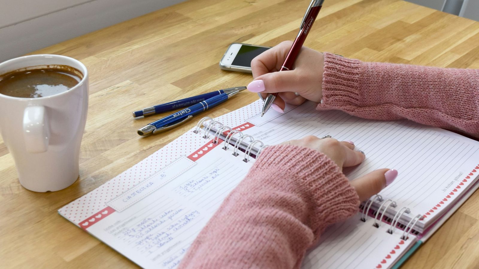 Person writing goals in a planner at a sunny desk with a cup of coffee