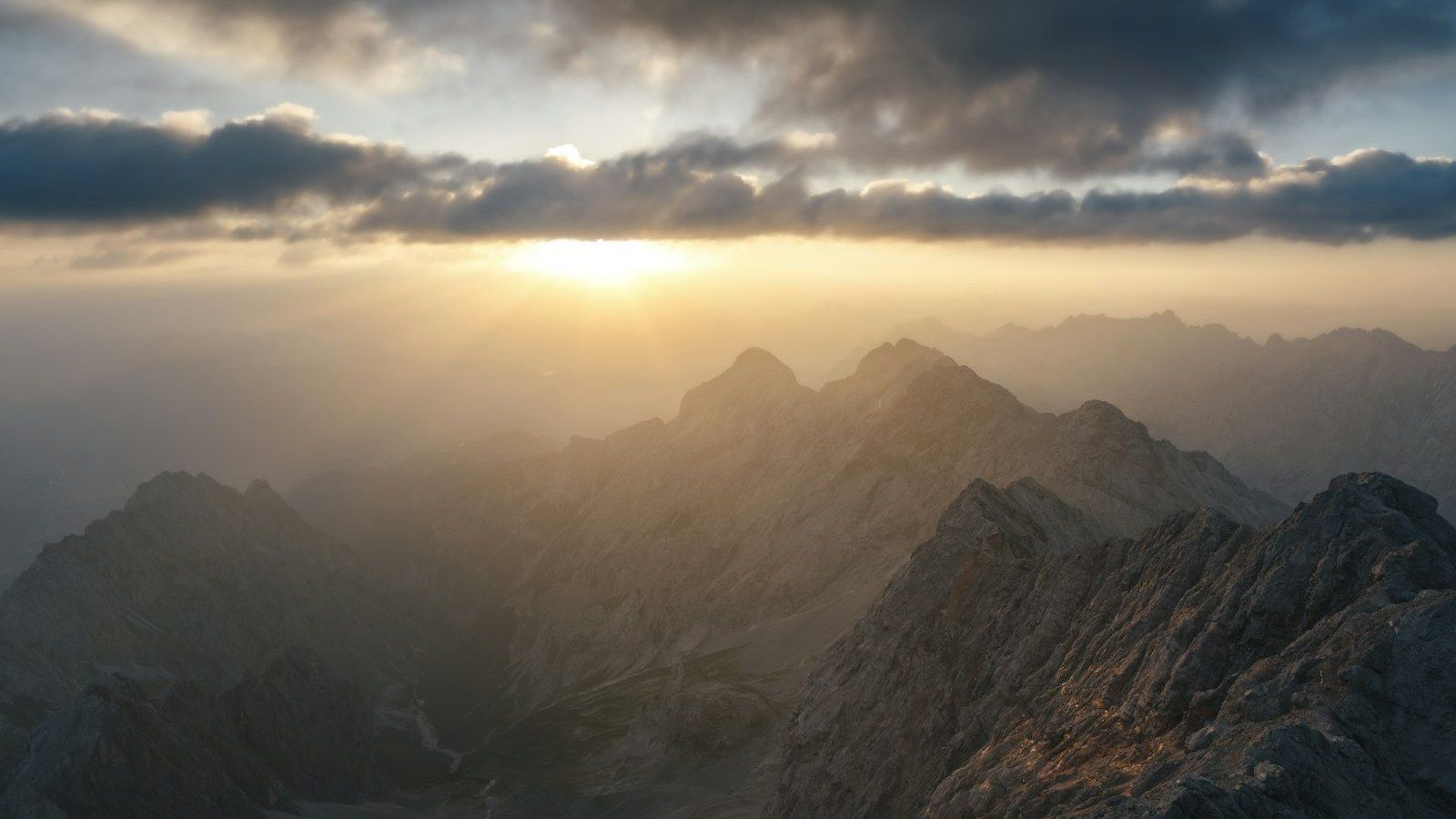 Morning sun breaks through clouds over rugged mountain peaks