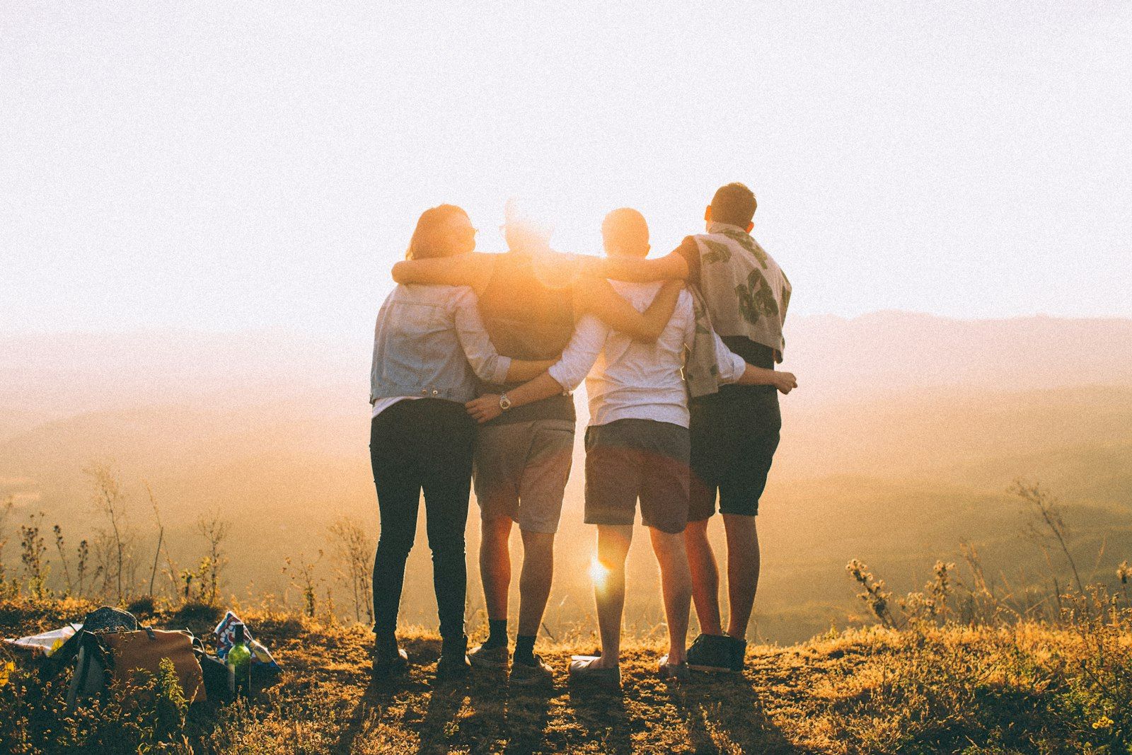 Four friends standing arm in arm together watching the sunset