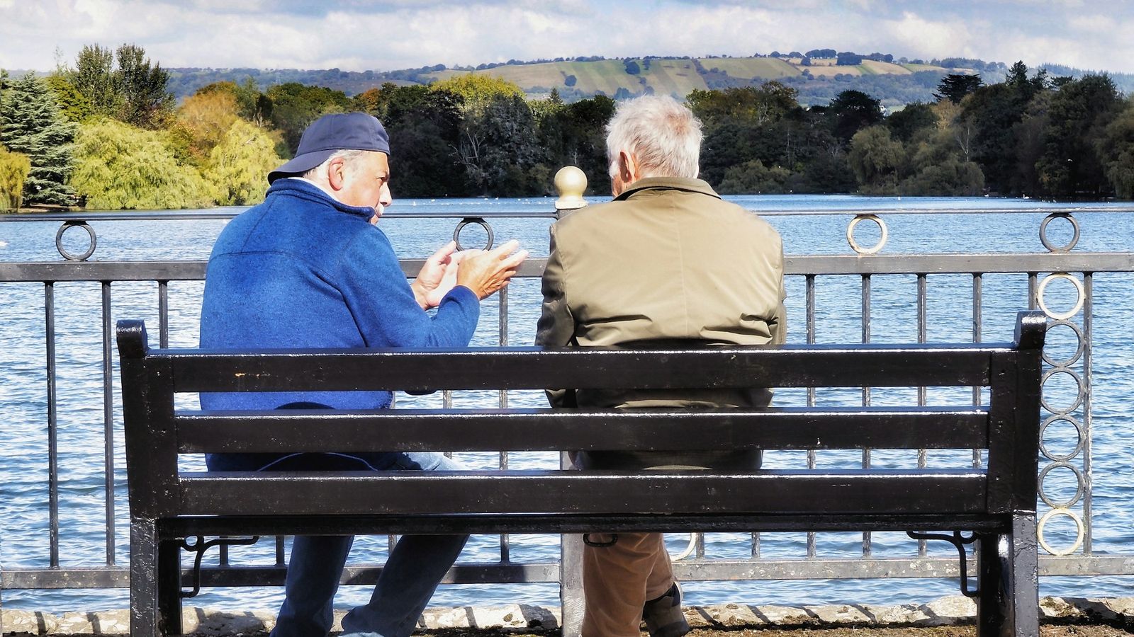 Two men having a supportive conversation on a lakeside bench