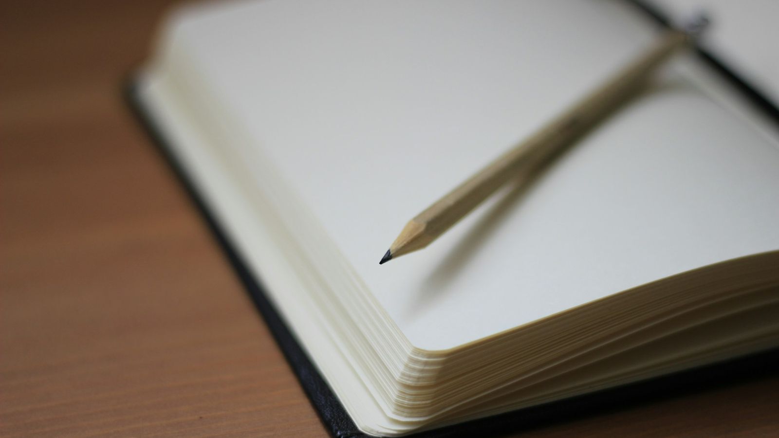 Open notebook with blank pages and a pencil resting on top