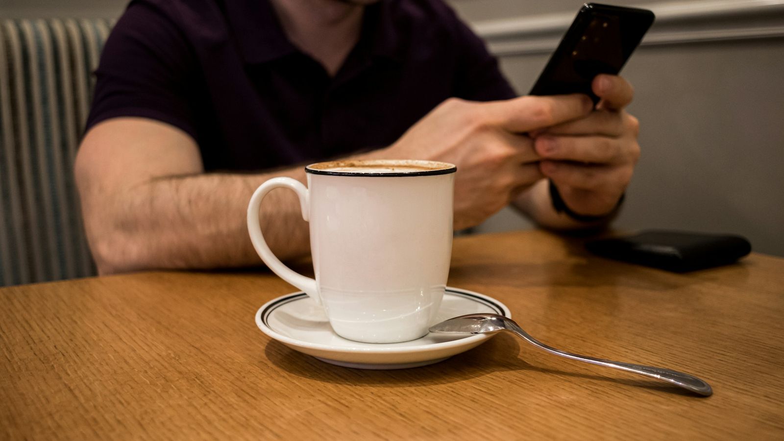 A man using a smartphone at a cafe table beside a cup of coffee