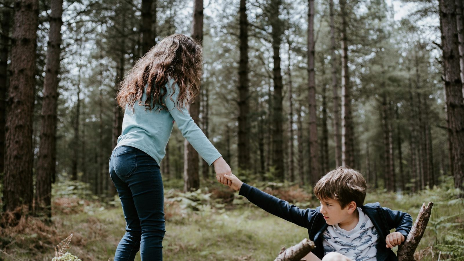 Older sister helping her younger brother climb over a fallen log in the woods