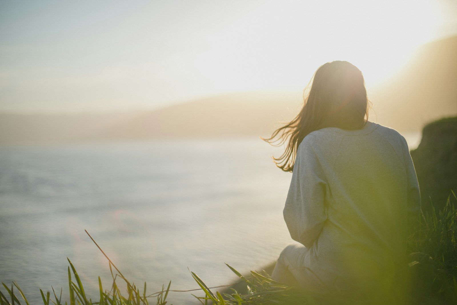 Woman sitting quietly by the water at sunrise, taking a calm moment outdoors