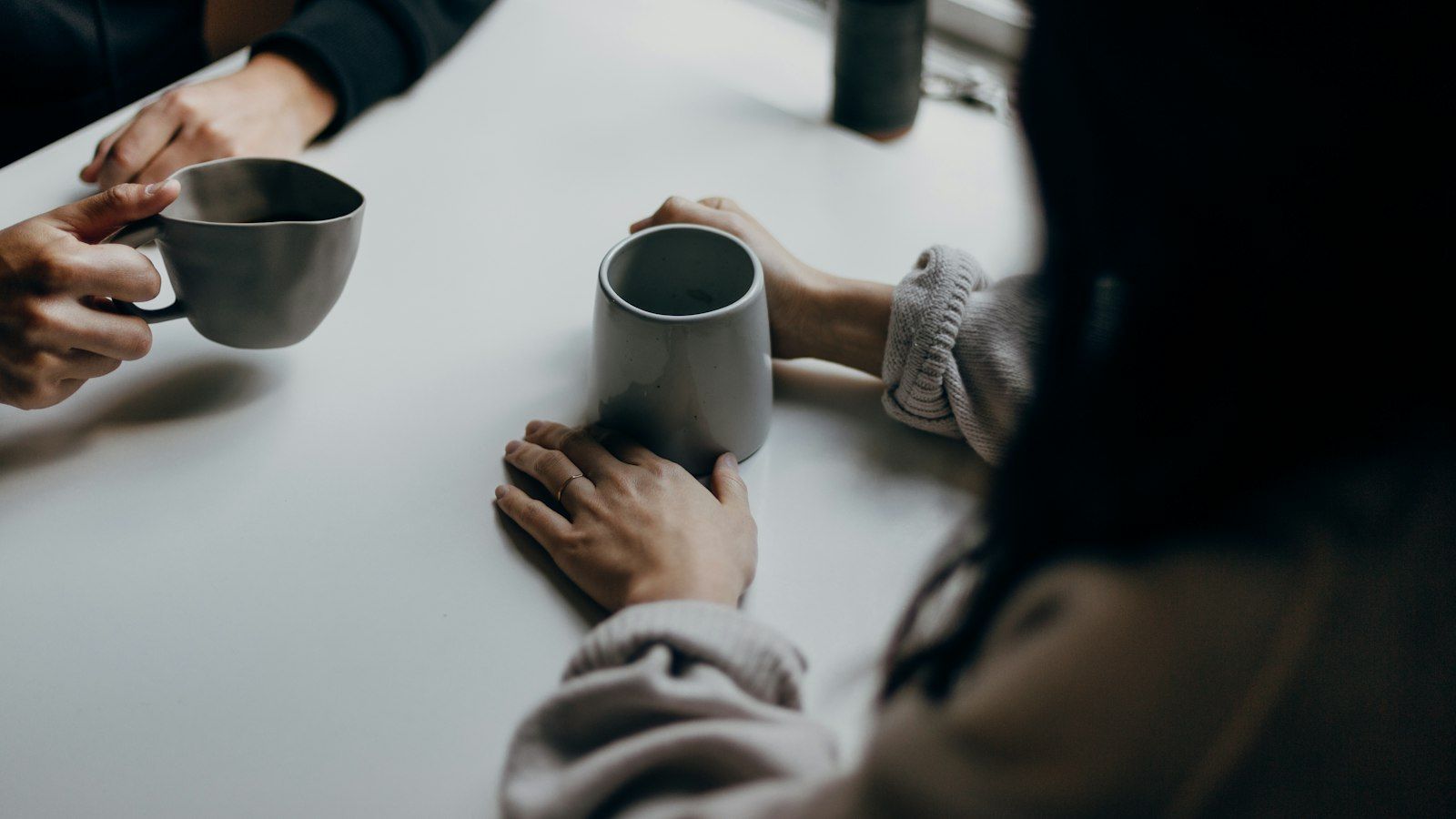 Two people talking over coffee mugs across a table