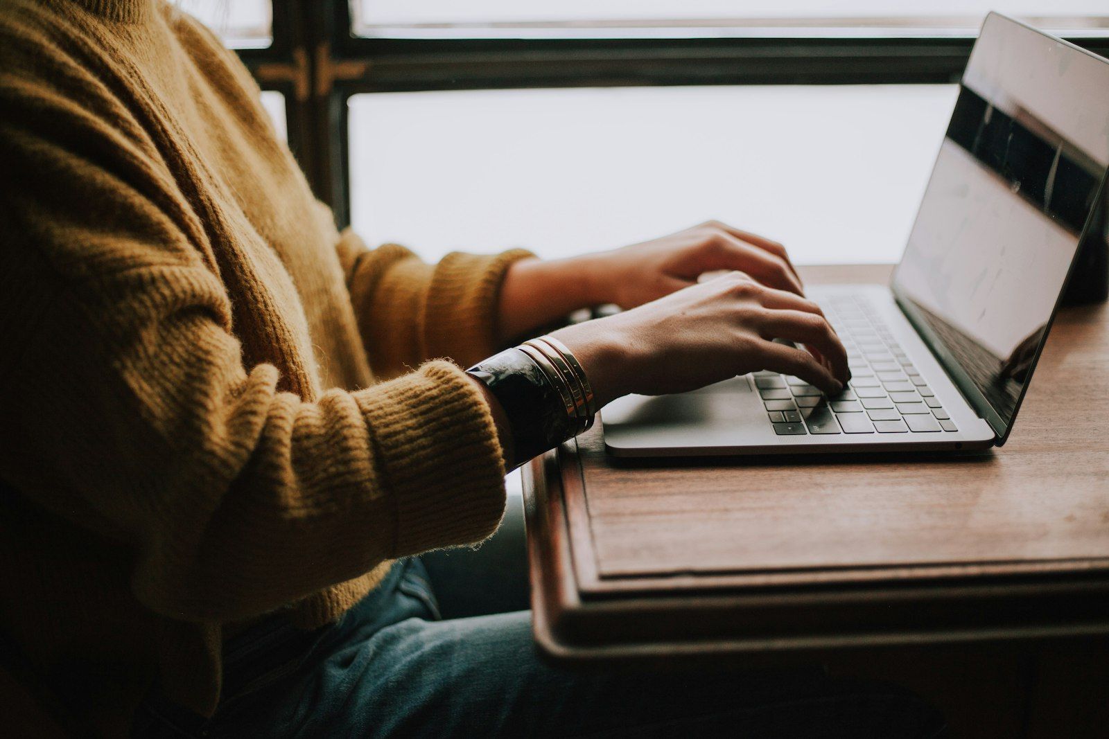 Person typing on a laptop at a desk by a bright window, getting started on a task