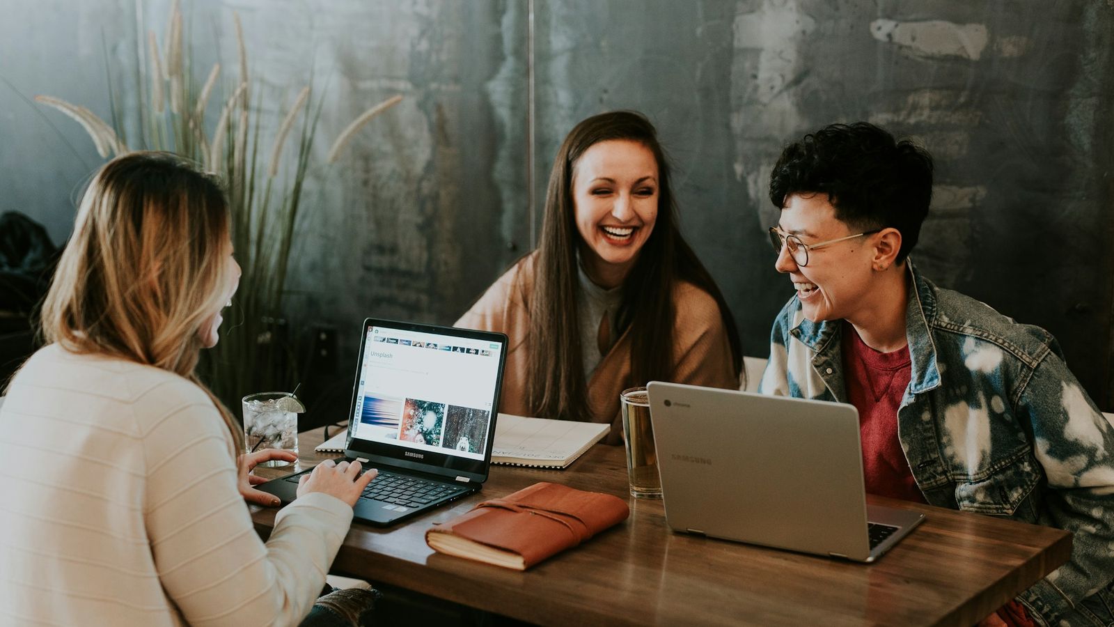 Three coworkers laughing and collaborating around a table with laptops