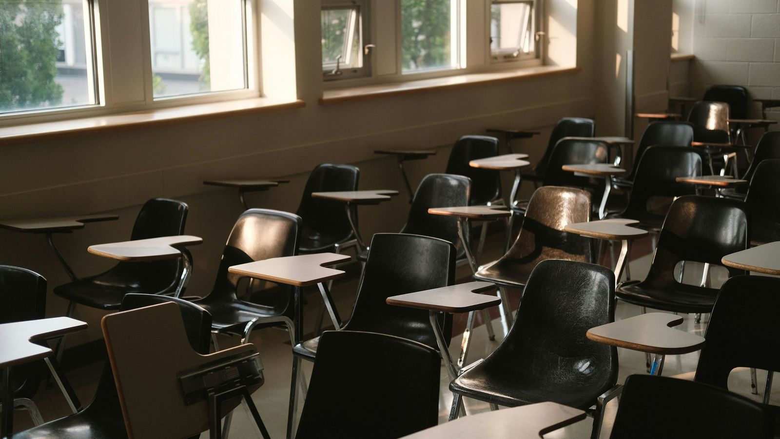 An empty classroom with rows of desks lit by sunlight from the windows