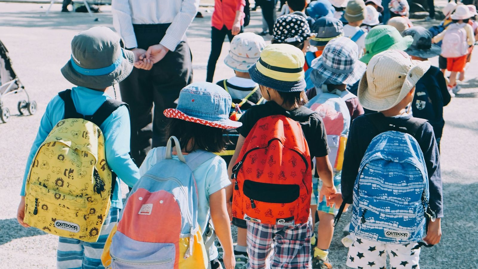 Young children with colorful backpacks walking to school together on a sunny morning