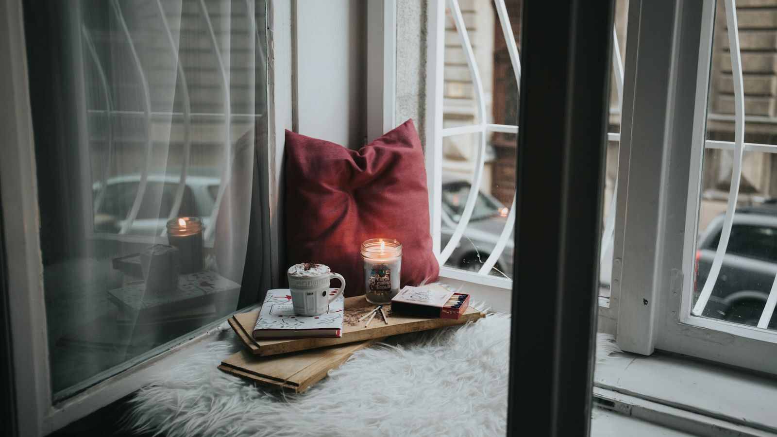 Cozy window seat with a lit candle, warm drink, and book on a winter day