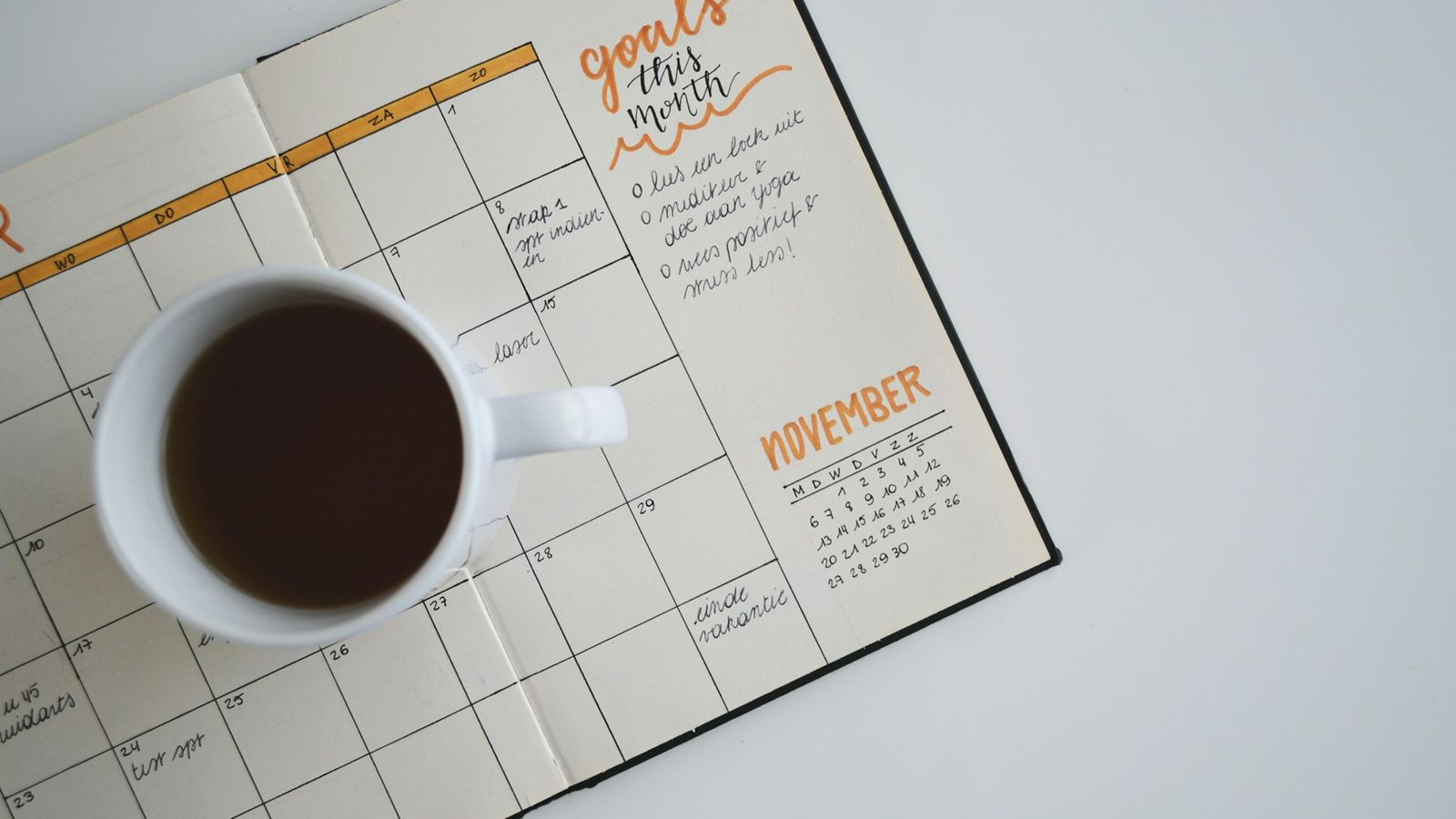 Cup of coffee resting on an open monthly planner with handwritten goals