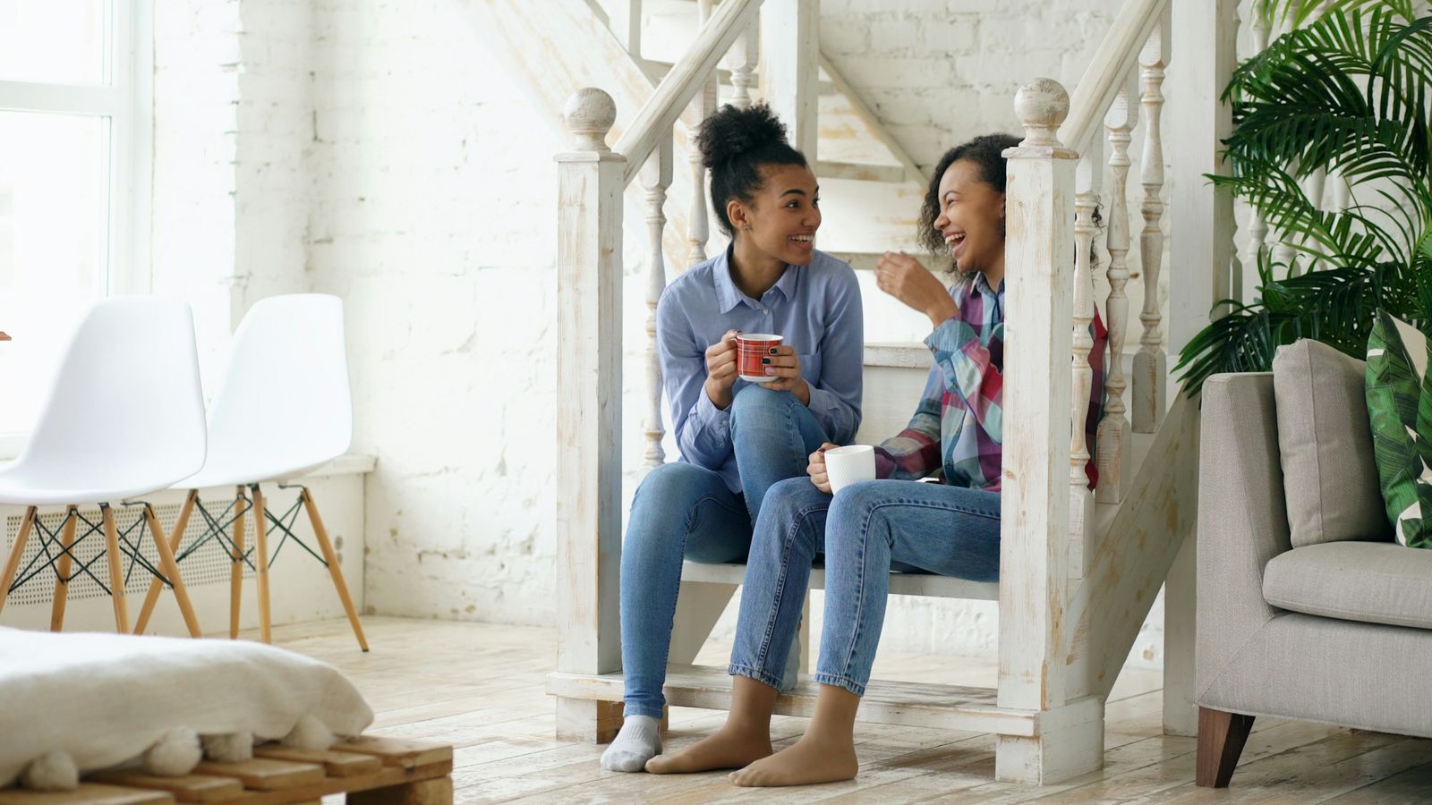 Two friends laughing together over coffee on a staircase
