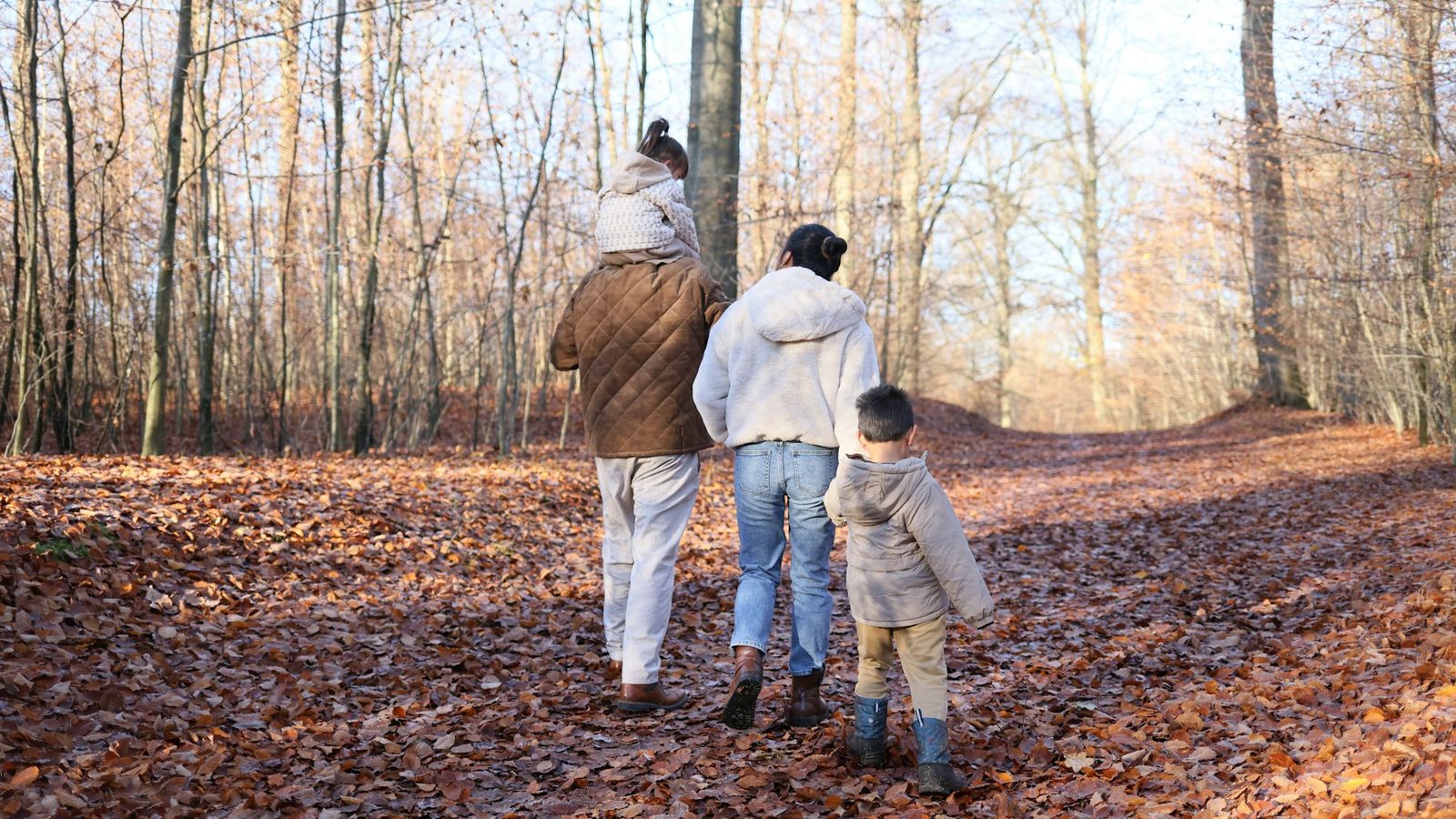 A family walking together down a leaf covered woodland path, seen from behind